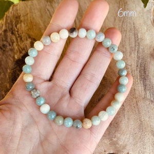 May include: A bracelet made of 6mm round, multi-colored, natural gemstone beads. The beads are shades of green, blue, and white. The bracelet is on a hand, and the text "6mm" is visible in the background.