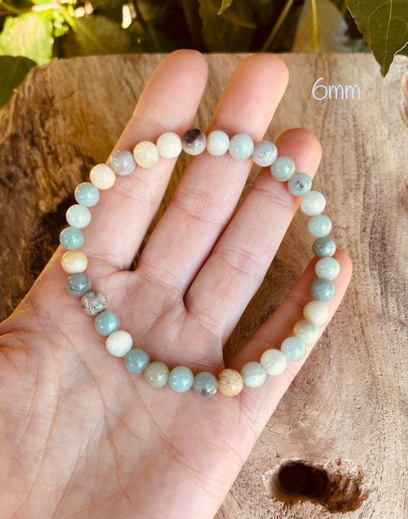 May include: A bracelet made of 6mm round, multi-colored, natural gemstone beads. The beads are shades of green, blue, and white. The bracelet is on a hand, and the text "6mm" is visible in the background.