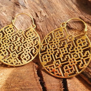 Peut inclure: Une paire de boucles d'oreilles créoles dorées avec un motif géométrique. Les boucles d'oreilles sont en métal et ont une forme circulaire.