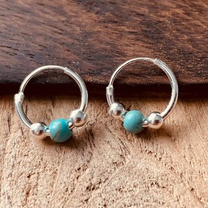 May include: A pair of silver hoop earrings with turquoise beads. The hoops are small and delicate, and the turquoise beads are a light blue color.