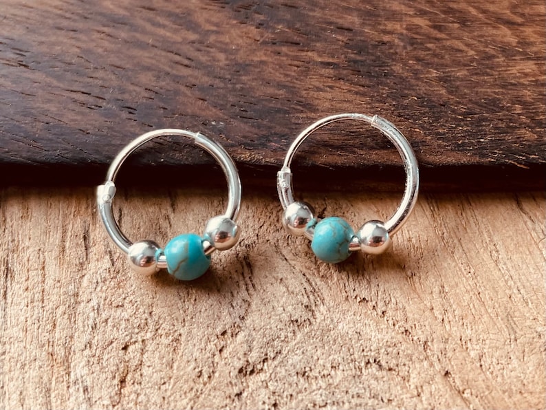 May include: A pair of silver hoop earrings with turquoise beads. The hoops are small and delicate, and the turquoise beads are a light blue color.