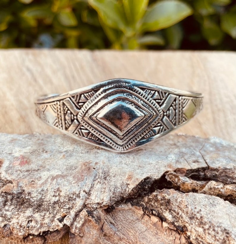 May include: A silver bracelet with a geometric design. The bracelet is made of metal and has a diamond-shaped center piece.