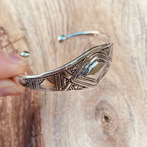 May include: A silver bracelet with a geometric design. The bracelet is made of metal and has a shiny finish.