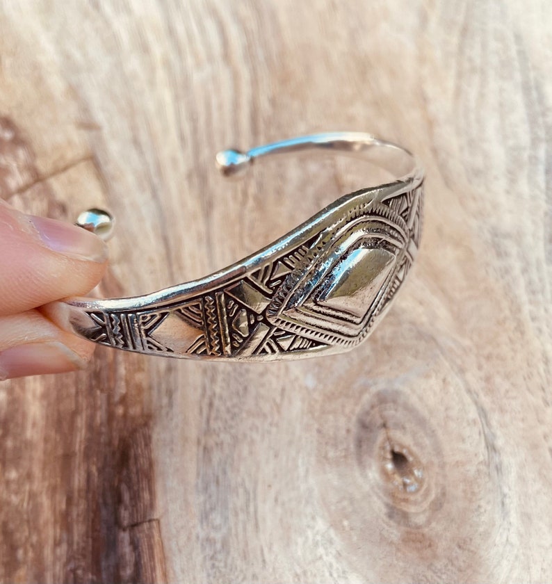 May include: A silver bracelet with a geometric design. The bracelet is made of metal and has a shiny finish.