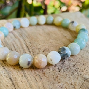 May include: A bracelet made of light green, white, and beige round beads. The beads are all about the same size and are strung together on a clear elastic cord.