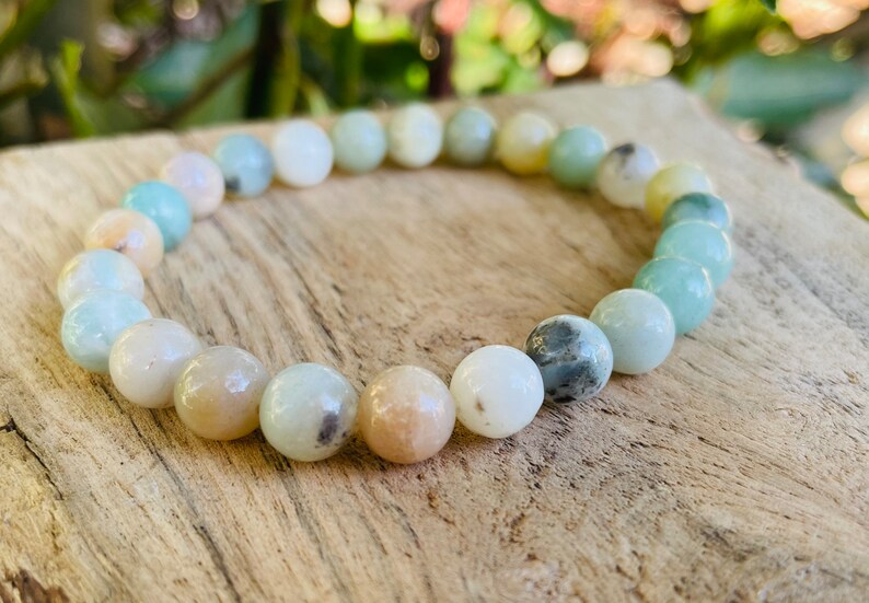 May include: A bracelet made of light green, white, and beige round beads. The beads are all about the same size and are strung together on a clear elastic cord.