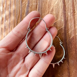 May include: Silver hoop earrings with a row of pointed spikes around the edge.