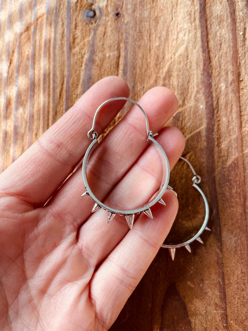 May include: Silver hoop earrings with a row of pointed spikes around the edge.