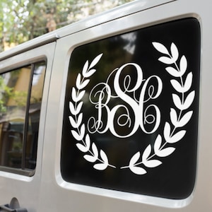 May include: White monogram decal featuring the letters BSC within a laurel wreath, affixed to a car window. The decal is a decorative item, possibly for personalising the vehicle.