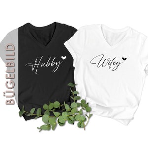 Könnte beinhalten: Zwei schwarze und weiße T-Shirts mit V-Ausschnitt. Das schwarze Shirt sagt "Hubby" mit einem weißen Herzen. Das weiße Shirt sagt "Wifey" mit einem schwarzen Herzen.
