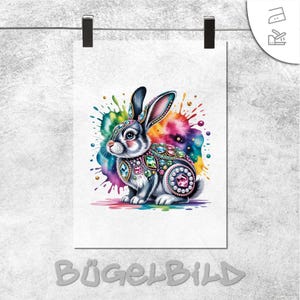 Può includere: Una stampa decorativa con un'illustrazione dettagliata di un coniglio adornato con gioielli colorati. Il coniglio è ambientato su uno sfondo vivace di acquerello multicolore. La parola "BÜGELBILD" è stampata in basso.