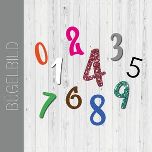 Puede incluir: Un conjunto de números para planchar en diferentes colores, incluyendo naranja, blanco, rosa, rojo, gris, negro, verde, marrón, azul y verde azulado. Los números están dispuestos en un patrón aleatorio sobre un fondo de madera blanca.