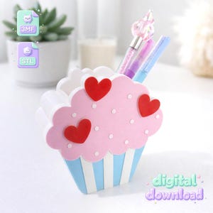 May include: A cupcake-shaped pen holder in pastel colors, featuring a pink top with red heart accents and white polka dots. The base is blue with white stripes. The holder contains pens and the words "digital download".