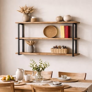 May include: A dining room scene featuring a wooden table set for a meal. Above, a three-tiered wooden shelf with black metal supports displays decorative items like vases, books, and a woven plate. The room is bright with natural light.