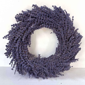May include: A circular wreath made of dried lavender. The wreath is a deep purple color and has a dense, textured appearance. The lavender is arranged in a circular pattern, creating a natural and rustic decorative item.