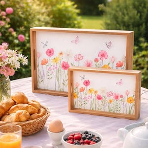 Puede incluir: Dos bandejas de madera con diseños florales, mariposas y libélulas. Las bandejas son rectangulares con un marco de madera clara. La escena incluye una mesa de desayuno con cruasanes, fruta y una tetera, al aire libre.