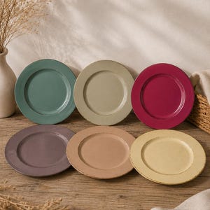 Può includere: Sei piatti in ceramica colorati nelle tonalità di verde, beige, bordeaux, viola, marrone chiaro e giallo. I piatti hanno una finitura rustica e invecchiata e sono disposti su una superficie di legno, suggerendo un tema di ristorazione.
