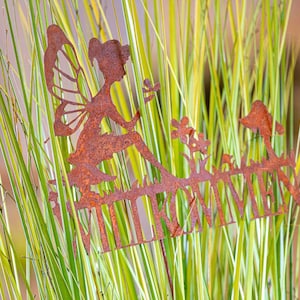 May include: A rusty metal fairy garden stake with a fairy silhouette holding a flower. The stake has the words "Welcome" written on it.