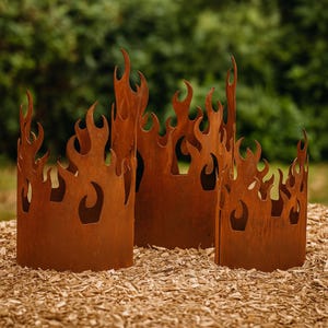 May include: Three rusty metal fire pit surrounds with flame cut-out designs. The outdoor decor is made of weathered metal and sits on a bed of wood chips. The flame-shaped cutouts create a unique visual effect.