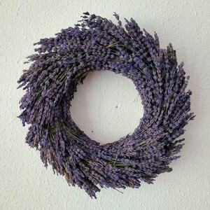 May include: A circular wreath made of dried lavender, showcasing a deep purple hue. The wreath is densely packed with lavender stems, creating a full and textured appearance. The wreath is a decorative item, perfect for adding a touch of natural beauty to any space.