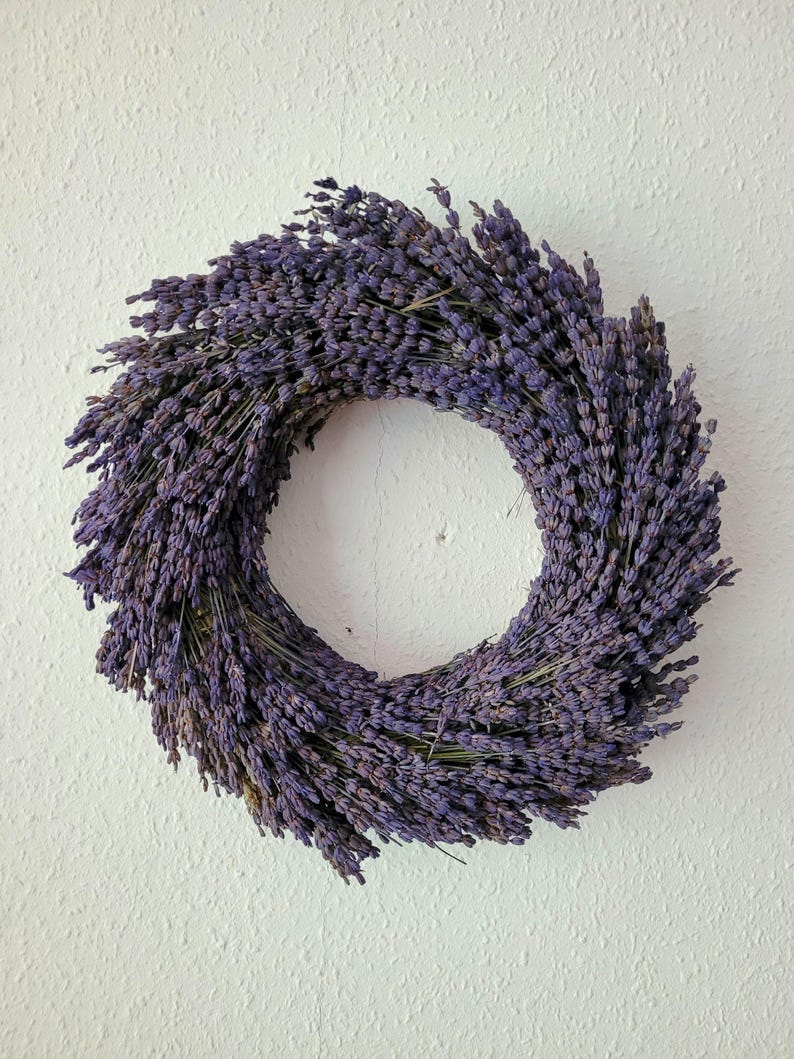 May include: A circular wreath made of dried lavender, showcasing a deep purple hue. The wreath is densely packed with lavender stems, creating a full and textured appearance. The wreath is a decorative item, perfect for adding a touch of natural beauty to any space.