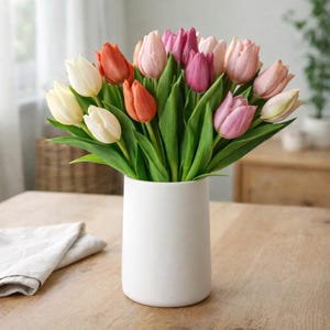 Könnte beinhalten: Ein Strauß bunter Tulpen in einer weißen Vase. Die Tulpen haben Farben wie Orange, Rosa, Lila und Weiß, mit grünen Stielen und Blättern. Die Vase steht auf einem Holztisch.
