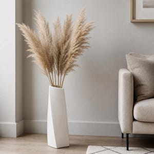 Può includere: Un vaso bianco alto, geometrico e con un design a spirale, che contiene un mazzo di pampas secche. Il vaso è posizionato su un pavimento in legno. Le pampas sono di colore beige chiaro, creando un'estetica neutra e naturale.