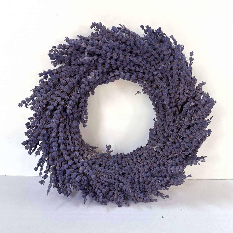 May include: A circular wreath made of dried lavender. The wreath is a deep purple color and has a dense, textured appearance. The lavender is arranged in a circular pattern, creating a natural and rustic decorative item.