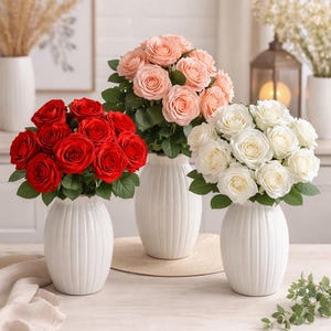 Könnte beinhalten: Drei weiße, gerippte Vasen mit Rosen. Eine Vase enthält leuchtend rote Rosen, eine weitere zart pfirsichfarbene Rosen und die dritte makellose weiße Rosen. Die Vasen stehen auf einem hellen Holztisch.