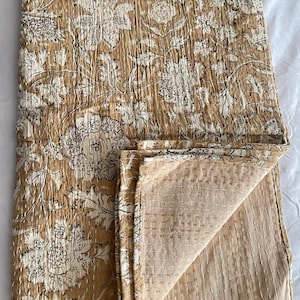May include: A brown and white floral kantha quilt with a hand-stitched design. The quilt is folded in half, showing the back side, which is a solid brown color.