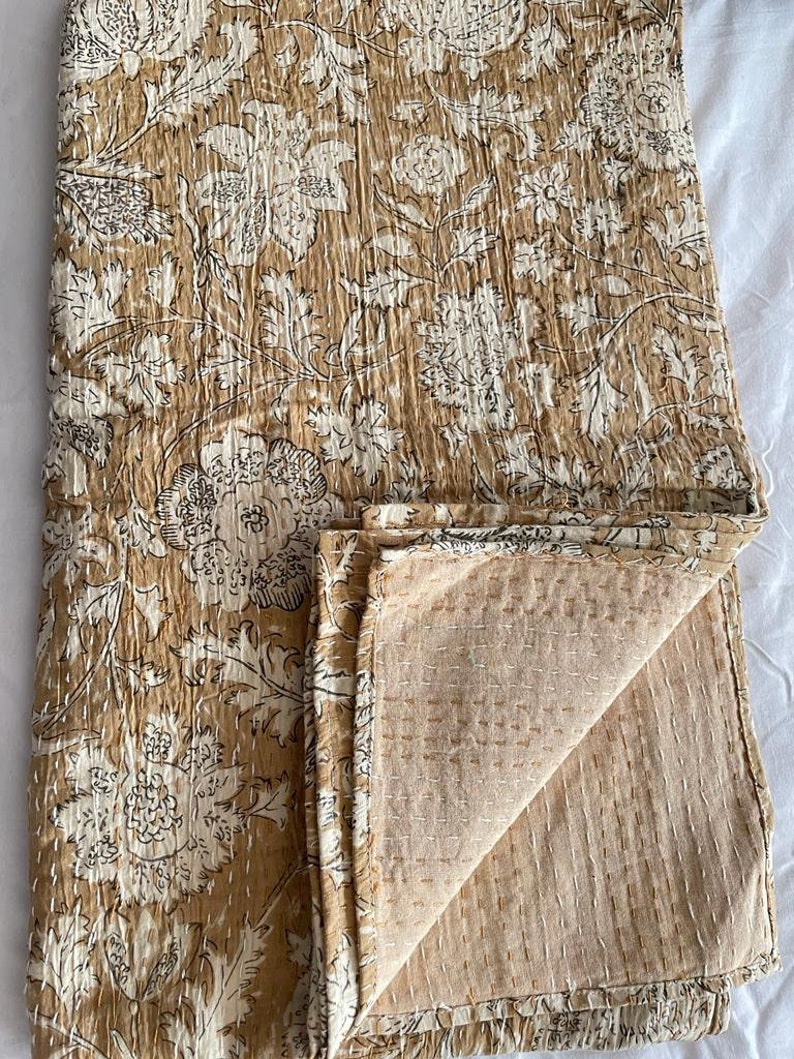 May include: A brown and white floral kantha quilt with a hand-stitched design. The quilt is folded in half, showing the back side, which is a solid brown color.