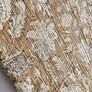 May include: A close-up of a brown fabric with a white floral pattern. The fabric has a textured surface and is made of cotton.