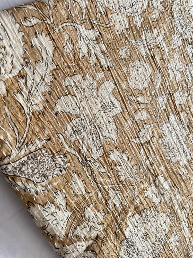 May include: A close-up of a brown fabric with a white floral pattern. The fabric has a textured surface and is made of cotton.