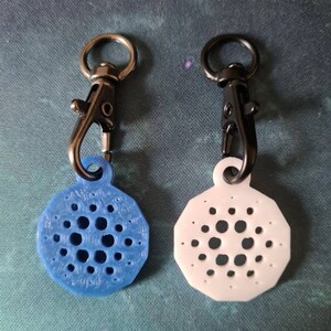 May include: Two keychains with a black swivel clip and a round, patterned charm. One charm is blue and the other is white.