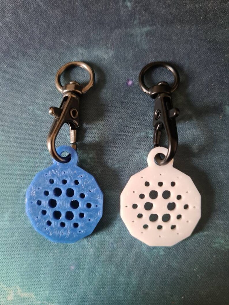 May include: Two keychains with a black swivel clip and a round, patterned charm. One charm is blue and the other is white.