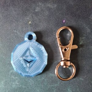 May include: A blue 3D printed keychain with the Ethereum logo and a silver metal key ring.