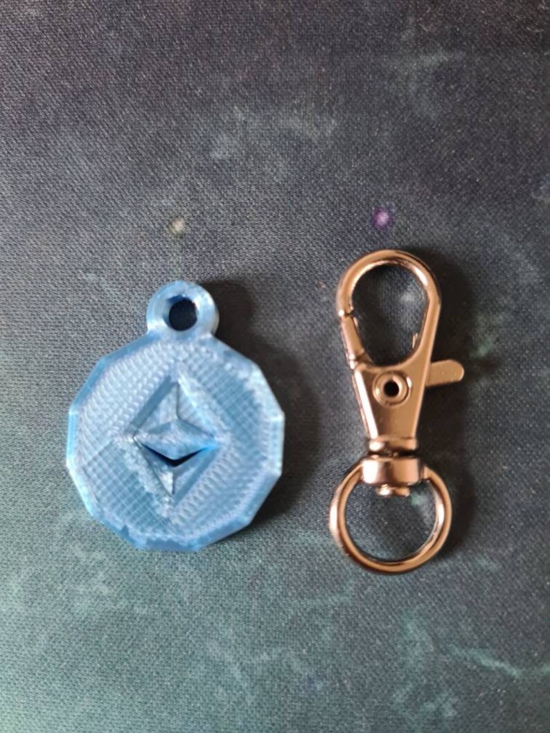 May include: A blue 3D printed keychain with the Ethereum logo and a silver metal key ring.