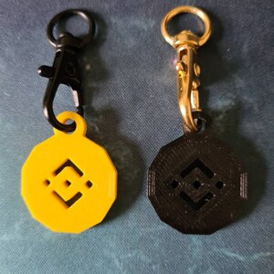 May include: Two keychains with a black and yellow logo. The keychains are made of metal and plastic. The logo is a stylized geometric shape.