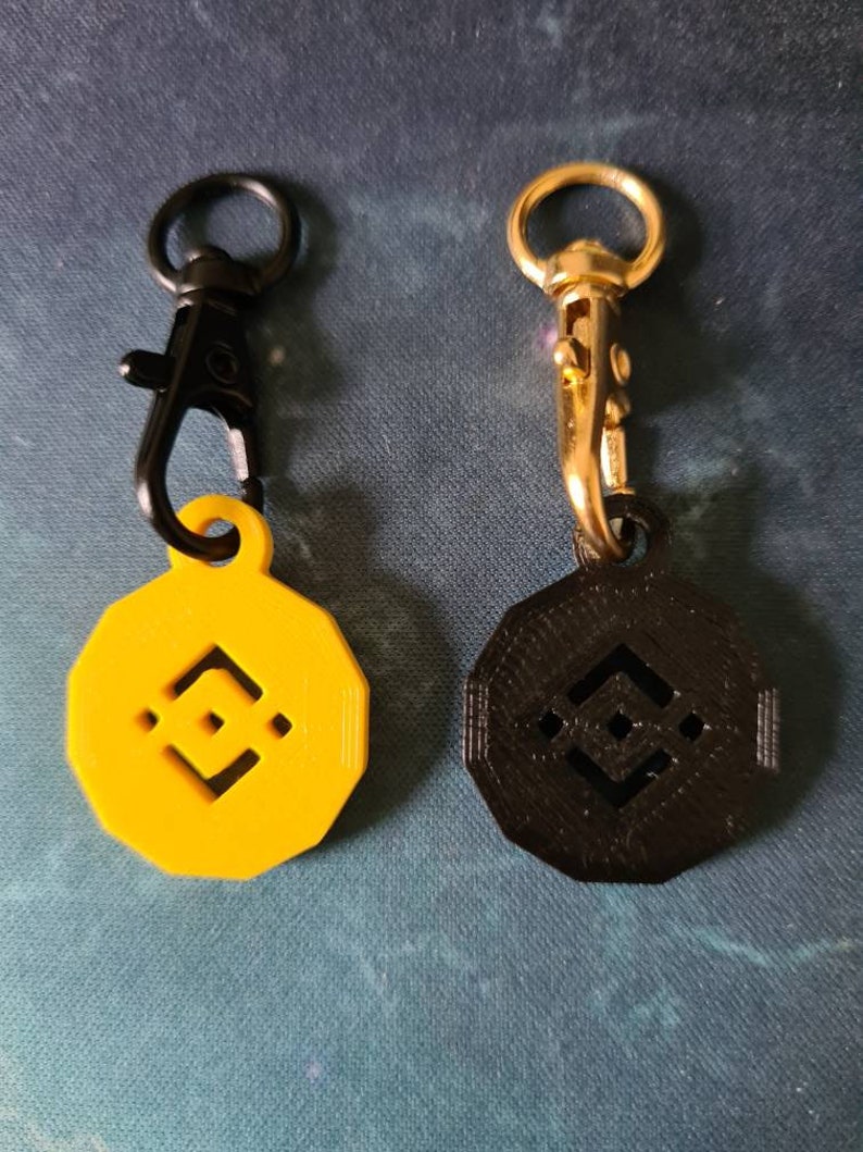 May include: Two keychains with a black and yellow logo. The keychains are made of metal and plastic. The logo is a stylized geometric shape.