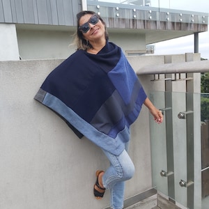 May include: A woman wearing a blue and black patchwork poncho with denim accents. She is wearing blue jeans and black sandals. The poncho is a casual and stylish piece of clothing.