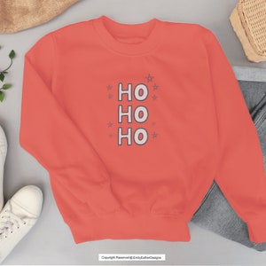 May include: Coral colored sweatshirt with the text "HO HO HO" in white with a black outline. The text is surrounded by small white stars.