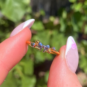 Può includere: Un anello d'oro con un piccolo ciondolo a forma di fiocco. Il fiocco è d'argento e ha una finitura testurizzata. L'anello è semplice e delicato.
