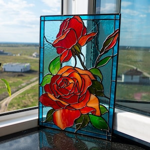May include: A stained glass window panel featuring two red roses with green leaves and stems on a blue background.