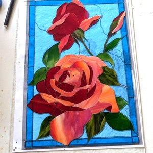 May include: A stained glass artwork featuring two red roses with green leaves on a blue background.