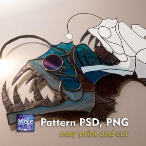 Op de afbeelding: Een kunstwerk van glas-in-lood van een diepzee-anglerfish met een bioluminescent lokmiddel. De vis is blauw, groen en bruin met een witte omtrek. De tekst "Pattern PSD, PNG easy print and cut" staat onder de vis.