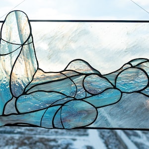 May include: A stained glass window depicting a stylized figure in a reclining pose, with blue and white glass pieces creating a wave-like pattern.
