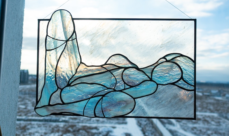 May include: A stained glass window depicting a stylized figure in a reclining pose, with blue and white glass pieces creating a wave-like pattern.