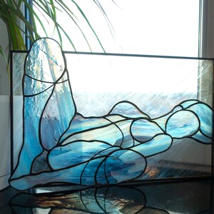 May include: A stained glass window depicting a stylized human figure in a reclining pose, with blue and white glass pieces forming the shape of the body.