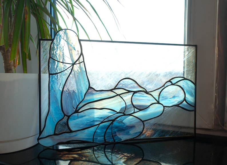 May include: A stained glass window depicting a stylized human figure in a reclining pose, with blue and white glass pieces forming the shape of the body.
