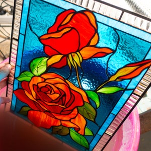 May include: A stained glass panel featuring two red roses with green leaves on a blue background. The panel is framed with a silver border.